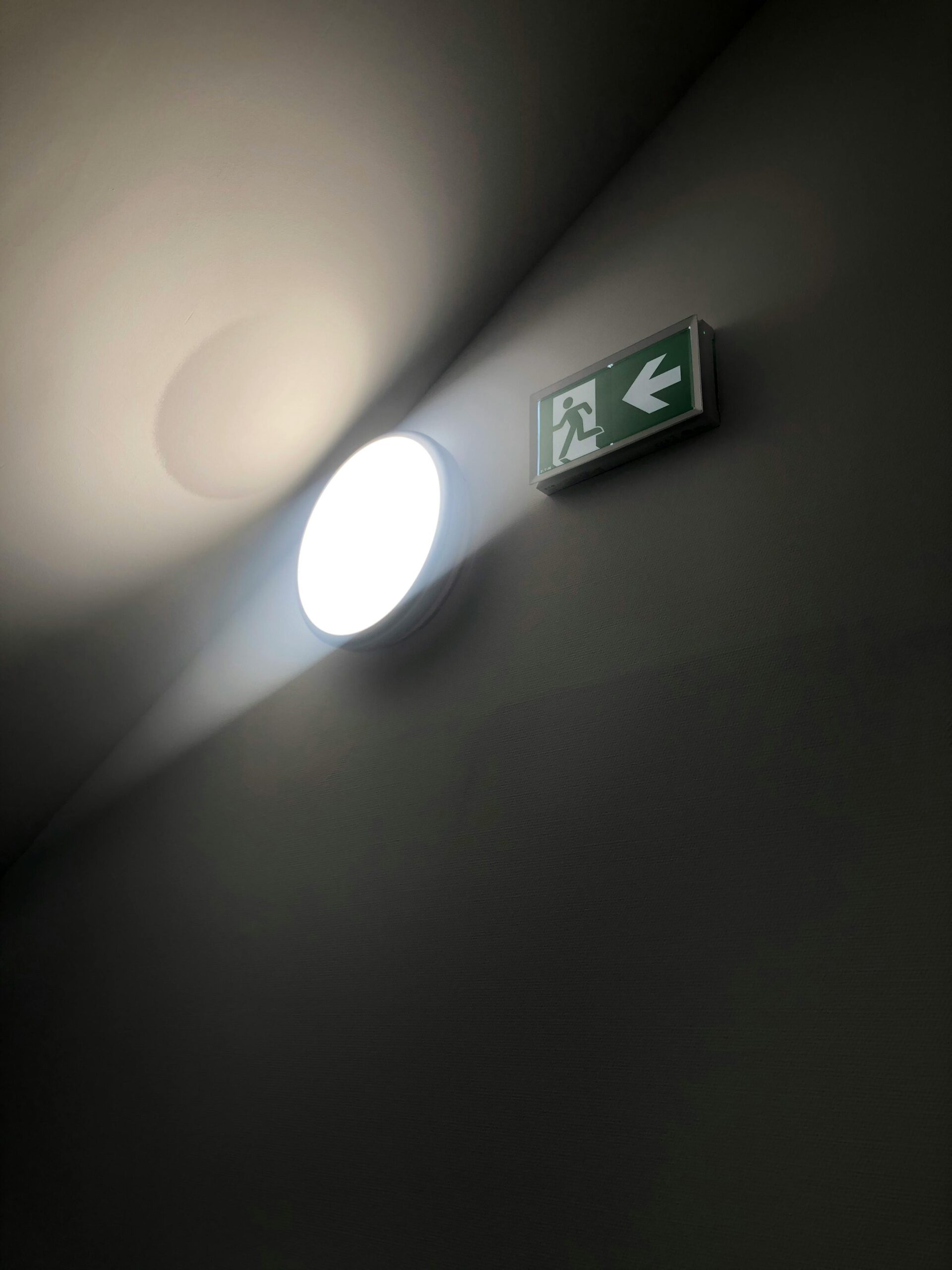 Illuminated emergency exit sign with light casting shadows on a dark wall.