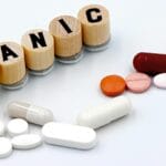 Assorted pills arranged beside wooden tiles spelling 'PANIC', symbolizing anxiety treatment.