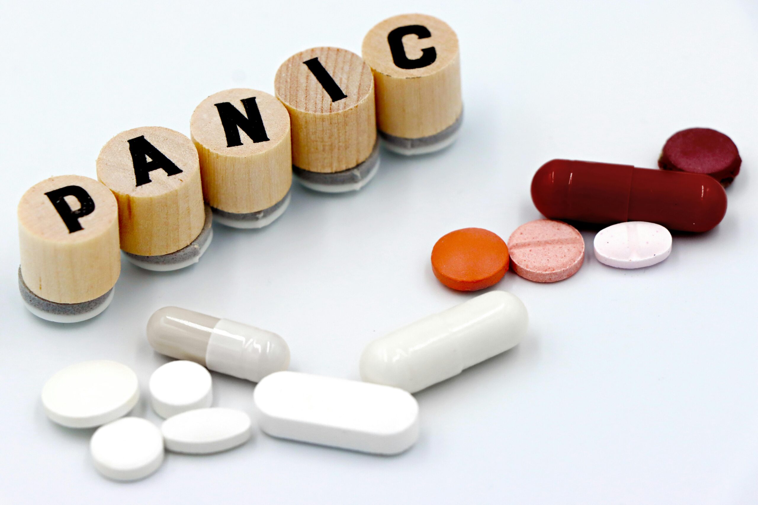 Assorted pills arranged beside wooden tiles spelling 'PANIC', symbolizing anxiety treatment.